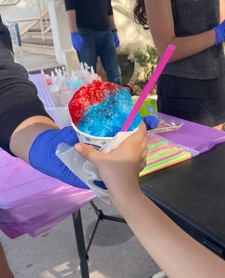 One of the students handing a red and blue snow-cone to another student.